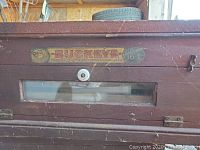 Front view of wooden Buckeye brand incubator showing glass window and capacity label for 16 eggs.