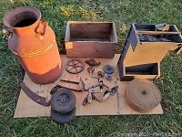 Overview of milk can, wooden box, metal grill, and assorted tools on cardboard outdoors.