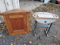 Front view of the wooden corner cabinet and the painted decorative table side by side on ground with fallen leaves.