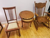 Photo of two rocking chairs and one round side table placed on wooden floor against white wall.