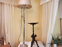 Full view of the floor lamp with shade and the small wood table side by side on a white surface.