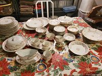 Wide view of the dish set on table showing all pieces including plates, bowls, cups, serving pieces with floral pink pattern and gold rims.
