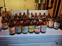 Front row of amber glass stout beer bottles showing brands: Labatt's, India Beer, Buckeye, Balatoni, Magnum Ale, Budweiser Budvar, Budweiser
