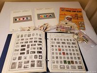 Full view of two souvenir collection postage stamp albums from 1978 and 1979, two blue binders with loose stamp pages, plastic bags containing loose stamps, and a vintage style Postage Stamp Album with astronaut on the cover.