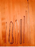 Photo of seven silver necklaces hanging vertically on a wooden background showing different chain styles and lengths.