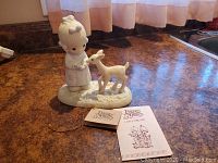 Photo of Precious Moments porcelain figurine next to its original tags on a countertop, showing the girl and deer figures.