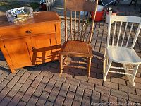 Photo showing the small wooden cabinet, two rocking chairs (one natural wood, one painted white), and faucet package on top of the cabinet.