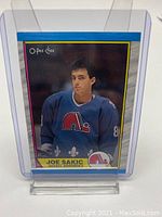 Front image of Joe Sakic in Quebec Nordiques uniform on 1989 O-Pee-Chee hockey card #113 held in protective case