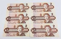 Front sides of six 1986 Canadian $2 banknotes arranged in two columns showing Queen Elizabeth II portrait and denomination 2 in brown tones.