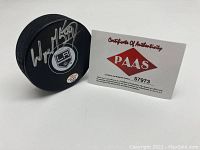 Hockey puck on its side showing Wayne Gretzky signature, LA Kings logo and PAAS authentication sticker alongside PAAS COA card