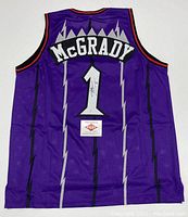 Back view of purple Toronto Raptors basketball jersey showing ‘McGrady’ nameplate, number ‘1’, autograph on number and PAAS COA card placed below.