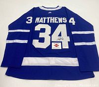 Back view of blue jersey displaying white number 34, 'Matthews' name, autograph on the '4', and PAAS COA card