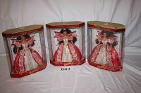 Three Barbie dolls displayed in original hexagonal boxes, dressed in red and white holiday themed gowns with gold trim.