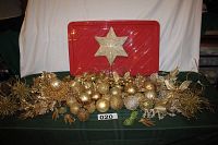 Full view of gold and glittery Christmas ornaments including tree topper, ball ornaments, branches, and leaves arranged on green cloth with red bin background.