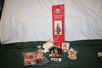 Photo of all items included in lot: decorated 24-inch tabletop tree in box, small Nativity, doll, two decorative houses, and bag of red/gold Christmas balls.