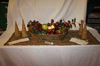 Full view of holiday table setup showing metal basket filled with artificial fruit and greenery, five gold glitter cone trees, table runner, and place cards.