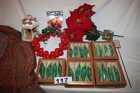 Display of all the items including four boxes each containing four green teardrop-shaped mercury glass ornaments, red jingle bell wreath, artificial poinsettias, Christmas fabric tablecloth, and other decorations.