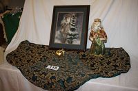 Full view of tree skirt laid flat showing green and gold fleur-de-lis pattern with braided edge, Victorian Santa statue standing next to framed Father Christmas picture and gold bell ornament on the skirt.