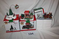 Image showing three Lemax Coventry Cove Christmas village items: animated flying Santa Christmas tree centerpiece on box, Christmas shop house on box, and vintage fire engine with firefighters and horses.