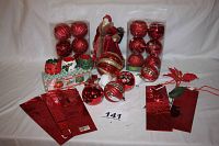 Full lot with red velvet Santa in center, two boxes of red large Christmas ball ornaments behind, additional loose red ornaments placed around, three red wine bags and a 3-piece candle set on left and right front.