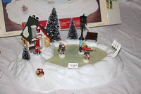 Full view of the animated skating pond set showing snow-covered base, pond, and figures including sledding child and small house