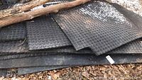 Stack of black rubber mats with circular coin pattern laid outdoors on leaves