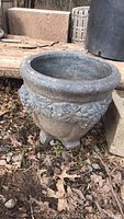 Side view showing decorative raised fruit and leaf pattern on round concrete planter.