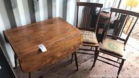 Wood drop leaf table and four square spindle back chairs with burlap seats shown together in used condition.