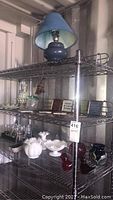 Metal shelf holding ceramic lamp on top shelf, glassware and pottery on bottom shelves