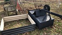 Wide view of metal planter bed partially assembled, with black trailer cart and other metal items on ground