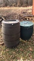 Two rain barrels outside on grass by wood pile, tallest barrel approximately 35 inches tall