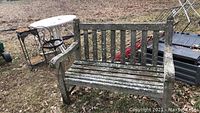Wood bench with moss and weathering sitting outdoors on grass and leaves, showing full view