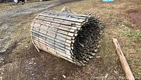 Roll of weathered wooden snow fence laid on ground, showing wooden slats and wire structure.