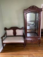 Full front view of carved wood cabinet with glass door next to bench for scale