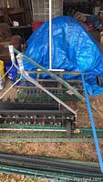 Photo showing trailer attachment tiller and aerator with metal tines and frame in front of blue tarp.