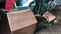 Two green wooden rush seat chairs and a vintage wooden feed bin shown in a rough storage area, displaying condition and style of each item.