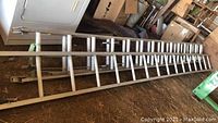 Full length view of the aluminum extension ladder laid flat on a barn floor, showing the entire section approximately 14 feet long.