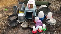 Overview photo of all chicken accessories including carriers, feeders, waterers and bowls showing various items arranged on ground.