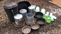 Full view of all chicken poultry feeders, waterers, bowls and large lockable black plastic storage bin arranged outdoors on gravel surface.
