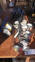 Photo showing a collection of assorted golf clubs laid out on a wooden surface, including drivers, irons and woods with metallic heads and black grips.