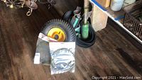 Photo showing green large hydraulic floor jack, green hydraulic bottle jack, rubber belts in sealed bags, and miscellaneous car parts on wooden floor.