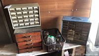 Group shot showing four storage units: two metal cabinets with multiple small drawers, one orange wooden drawer unit, and a plastic basket containing jars and bags of fasteners on a wooden surface.