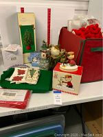 Overview of Christmas decor items arranged on a shelf; shows figurines, fabric pieces, ribbon rolls, and a red storage box.