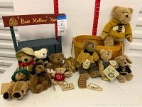 Front view showing all plush bears arranged with the wooden Bear Hollow Honey stand and basket behind, displaying size range and tags on most bears.