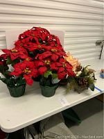 Two silk poinsettias with red petals and green base, plus two additional floral arrangements on white table.