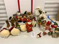 Overview of assorted Christmas figurines including plush Boyds Bears snowmen, ceramic Santas, and other holiday decorations arranged on a table.