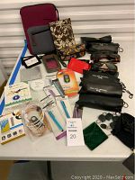 Full assortment of travel and tech accessories displayed on table including Polar Optics sunglasses, Vera Bradley items, cables, and locks.