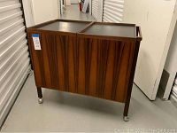 Three-quarter front view showing wood grain, vertical slatted front panels, handle, and caster wheels