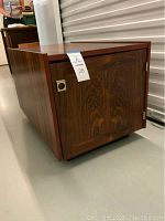 Side view of the wooden Danish modern style table showing closed cabinet door with metal pull handle and visible hinges.