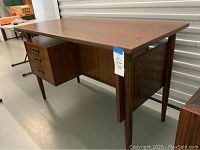 Front left three-quarter view showing desktop, left-side drawer bank, tapered legs